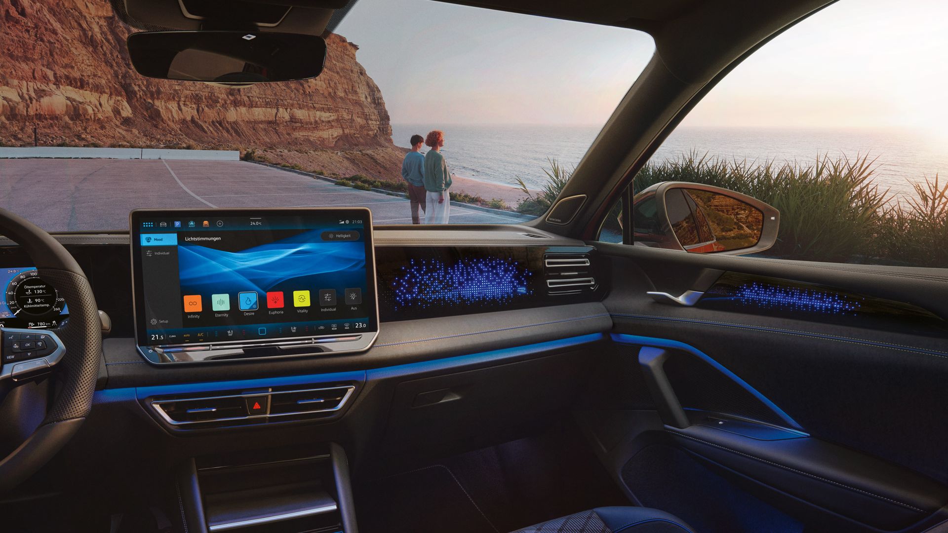 VW Tiguan mit blauer Ambientebeleuchtung. Durch die Frontscheibe ist ein Küstenlandschaft und ein auf das Meer schauendes Paar sichtbar.