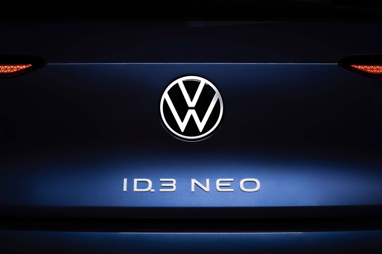 Nahaufnahme des Hecks eines Volkswagen ID.3 NEO. Im Zentrum ist das Volkswagen-Logo beleuchtet, darunter steht der Schriftzug "ID.3 NEO". Die Rücklichter sind auf beiden Seiten des Logos sichtbar.