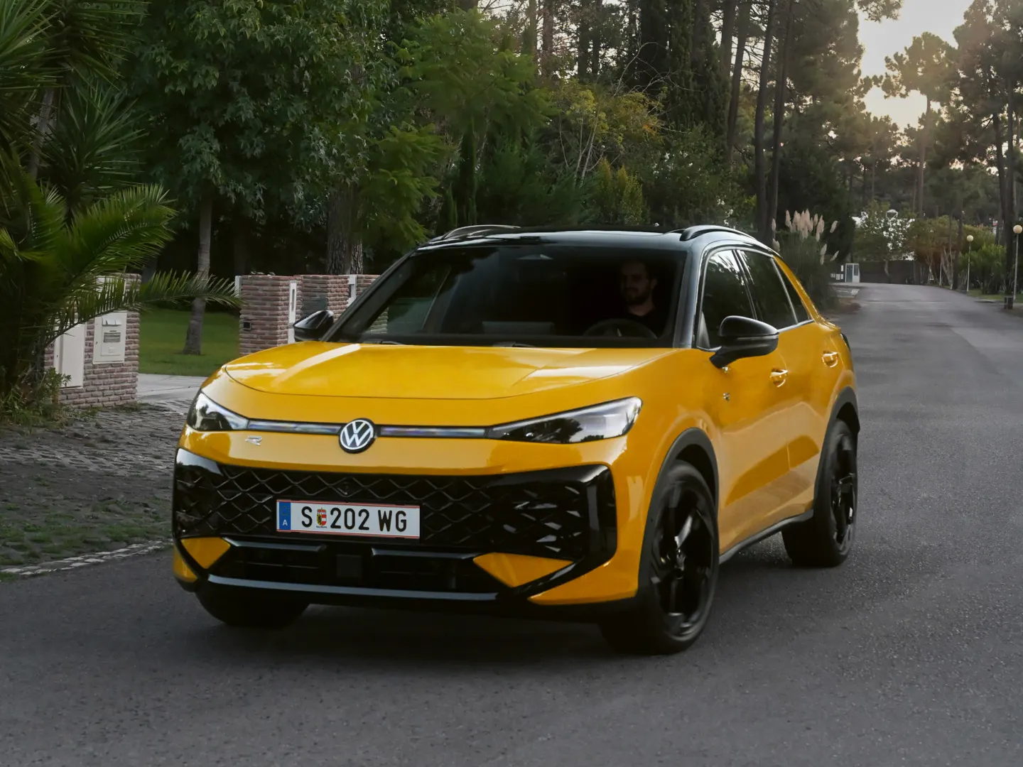 Ein gelber VW T-Roc R-Line fährt auf einer Straße durch eine bewaldete Umgebung.