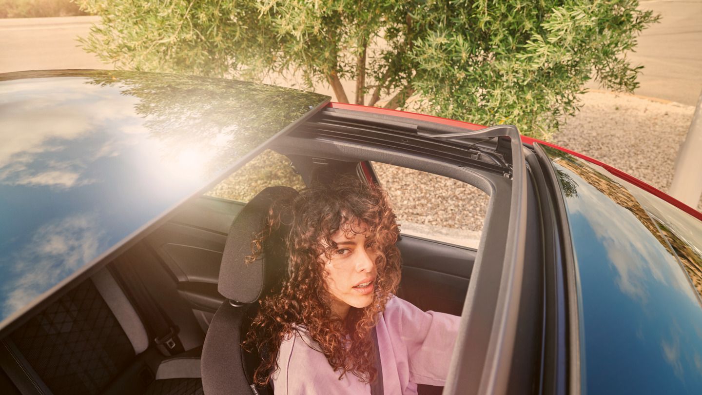 Blick von oben auf VW Taigo mit offenem Panorama-Ausstell-/Schiebedach. Eine Frau schaut von innen heraus.