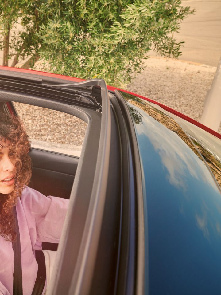 Blick von oben auf VW Taigo mit offenem Panorama-Ausstell-/Schiebedach. Eine Frau schaut von innen heraus.