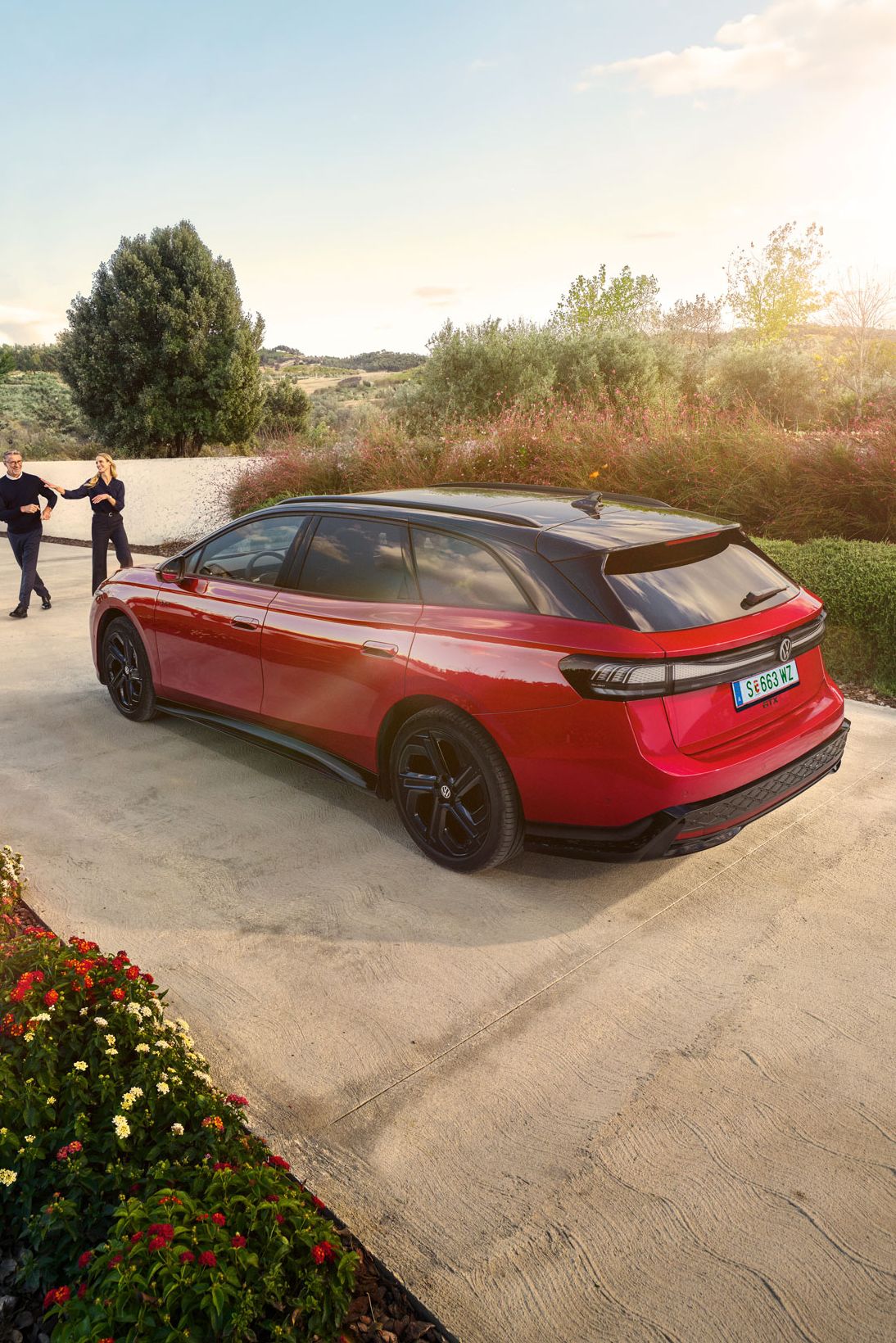Ein roter VW ID.7 GTX Tourer parkt in einer langen Auffahrt, ein Mann und eine Frau wollen einsteigen.