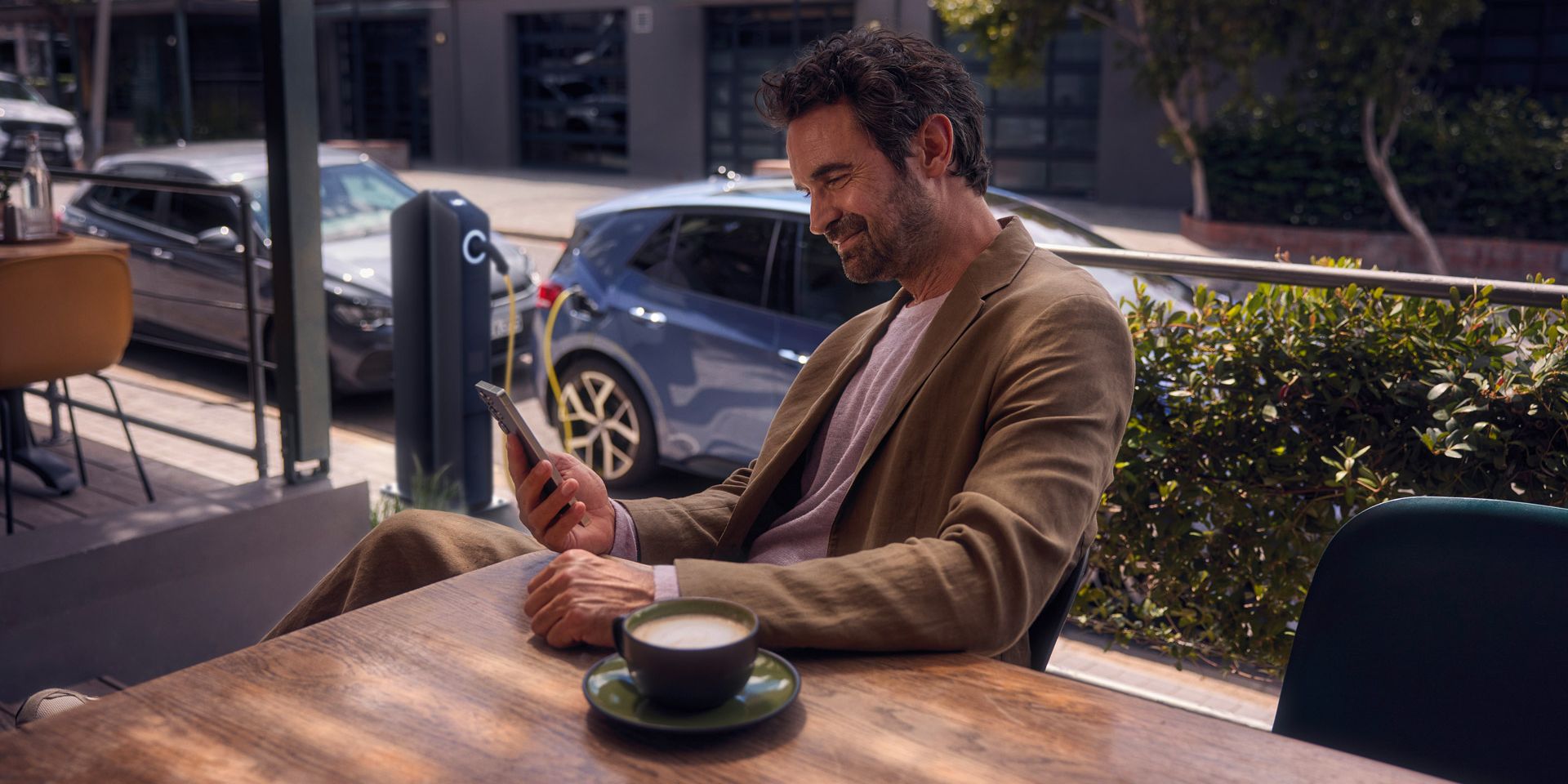 Ein Mann sitzt im Café und checkt per Smartphone den Ladestatus seines VW ID.3 Neo