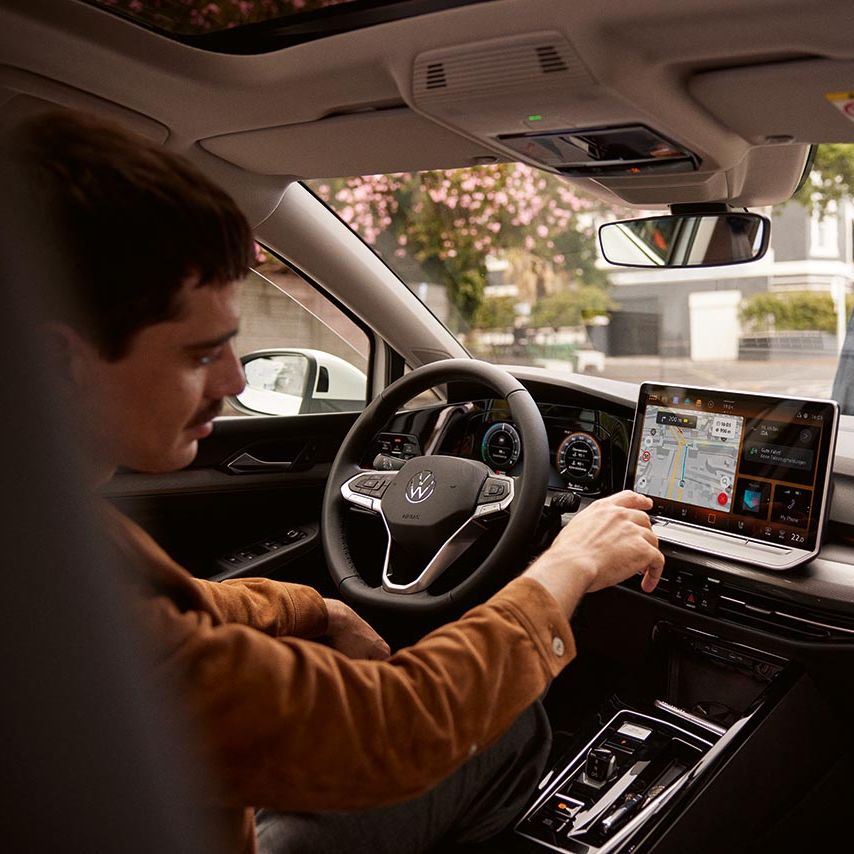 Ein Mann sitzt im parkenden VW Golf und bedient das Navigationssystem.
