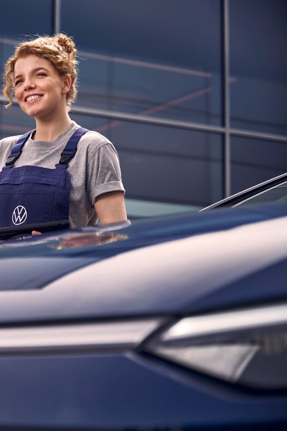 Eine Volkswagen Technikerin vor einer Volkswagen Werkstatt.