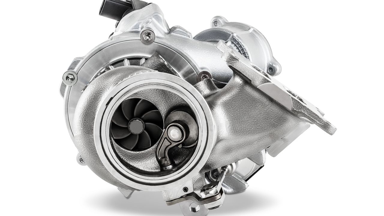 Ein metallischer Turbolader für einen Verbrennungsmotor, freigestellt vor weißem Hintergrund. Deutlich sichtbar sind das Gehäuse, das Verdichterrad mit seinen Schaufeln und der Abgasanschluss.