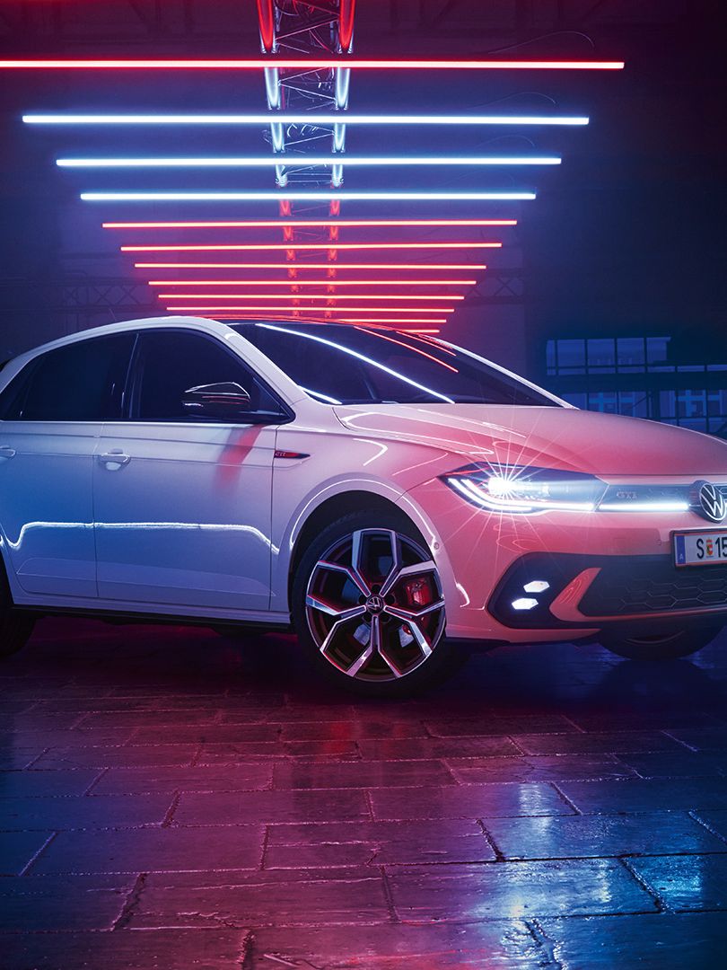 Ein weißer VW Polo GTI mit aktiven Scheinwerfern in einer dunklen Lagerhalle.