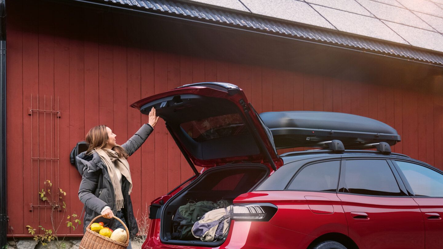 Eine Frau mit einem Korb voll Gemüse in der Hand steht vor der offenen Heckklappe eines roten VW ID.7 GTX Tourer.