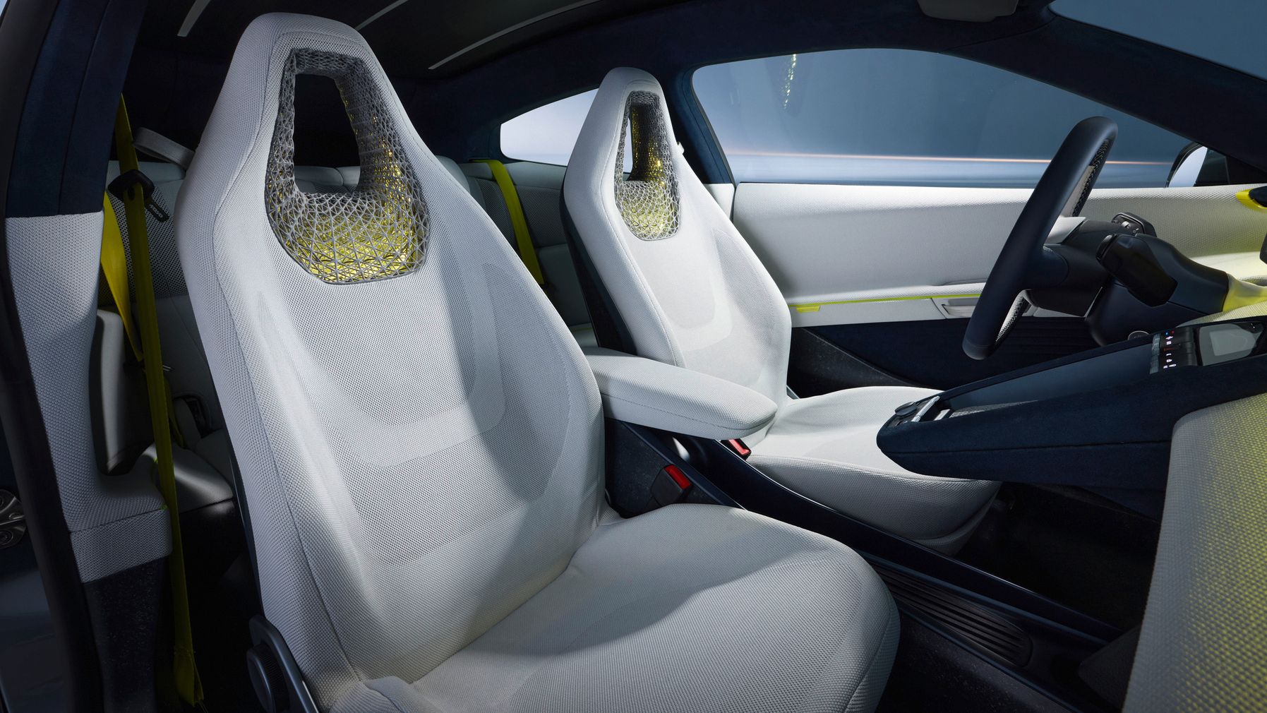 Innenraum eines modernen Autos mit zwei hellen, futuristisch gestalteten Vordersitzen mit integrierten Kopfstützen und wabenartiger Struktur. Die Mittelkonsole ist schlank und minimalistisch, mit einem schmalen, dunklen Armaturenbereich. Das Design wirkt aufgeräumt, technisch und auf sportliche Optik ausgerichtet.