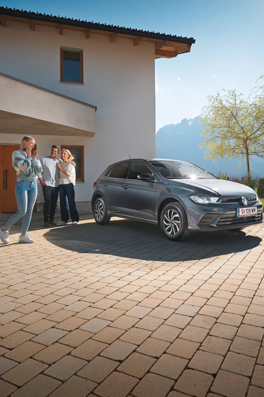 Polo steht geparkt vor einem Haus mit einer Familie im Hintergrund.