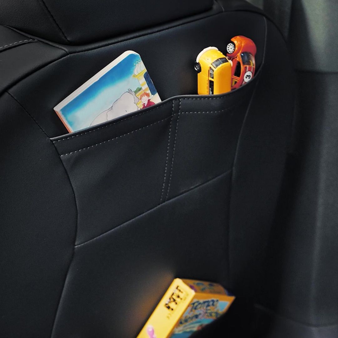 Eine schwarze Rücksitztasche im Auto enthält ein Kinderbuch, zwei kleine Spielzeugautos und ein gelbes Kartenspiel.