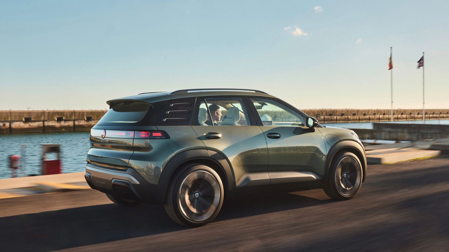 Ein grüner ID. Cross fährt auf einer Straße entlang der Küste. Im Hintergrund sind einige Flaggen und ein Hafengebiet zu sehen.