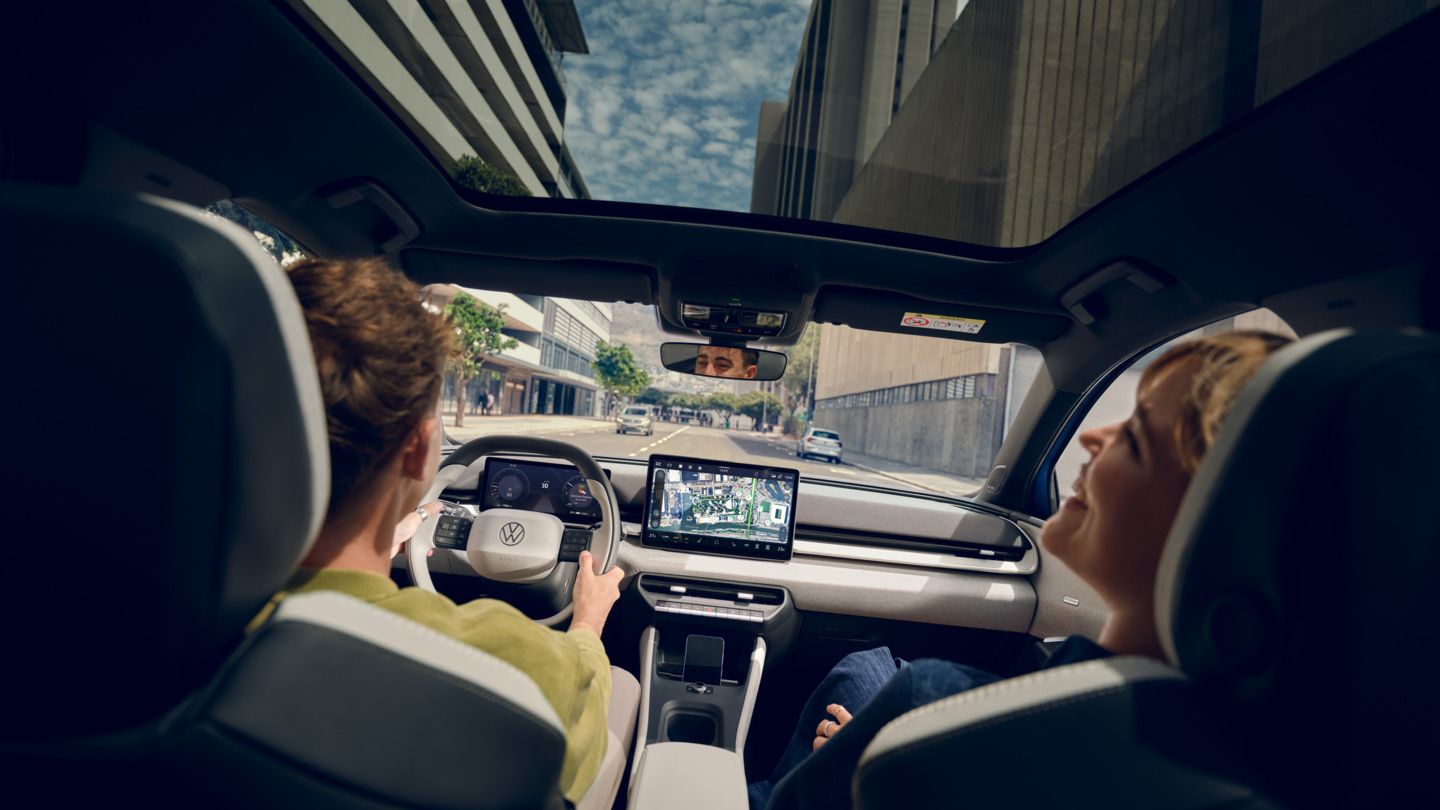 Ein Mann fährt einen VW ID. Polo Style, auf dem Beifahrersitz eine Frau die lacht. Durch das Panoramadach sind Hochhäuser zu sehen