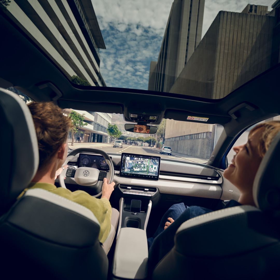 Ein Mann fährt einen VW ID. Polo Style, auf dem Beifahrersitz eine Frau die lacht. Durch das Panoramadach sind Hochhäuser zu sehen