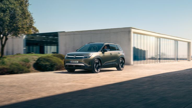 Ein grüner VW ID. Cross fährt auf einer Auffahrt eines modernen Wohngebäudes.