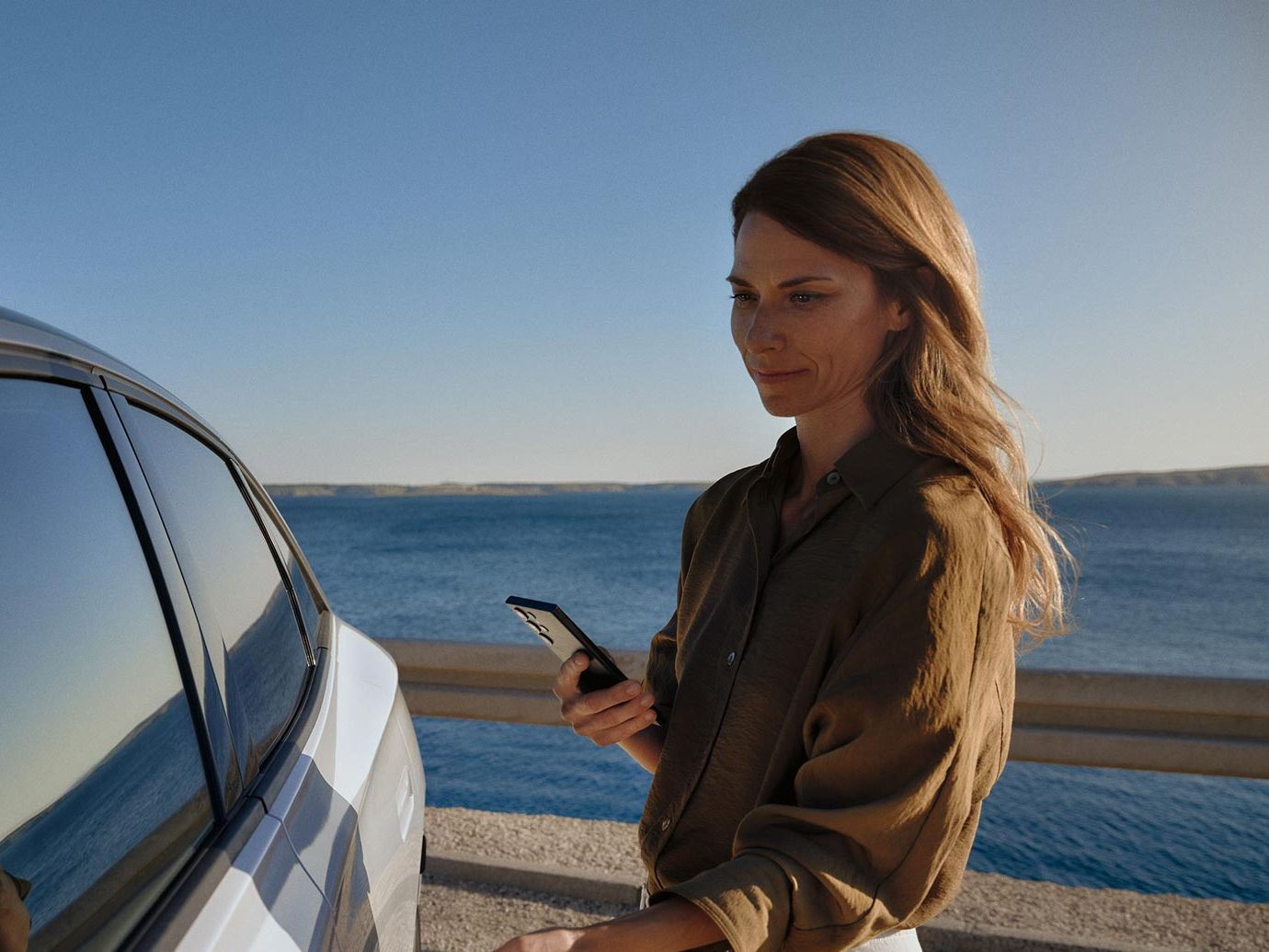 Eine Frau geht zu einem weißen VW ID.7 und öffnet die Tür. 