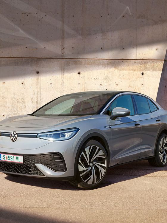 Grauer VW ID.5 parkt vor heller Hauswand, Ansicht schräg rechts von vorn, Mann geht zügig auf das E-Auto zu.