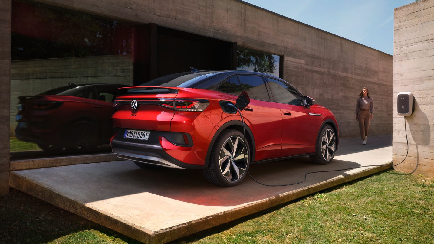 Ein roter VW ID.5 GTX lädt an einer Wallbox neben einem Bungalow mit großer Glasfront.