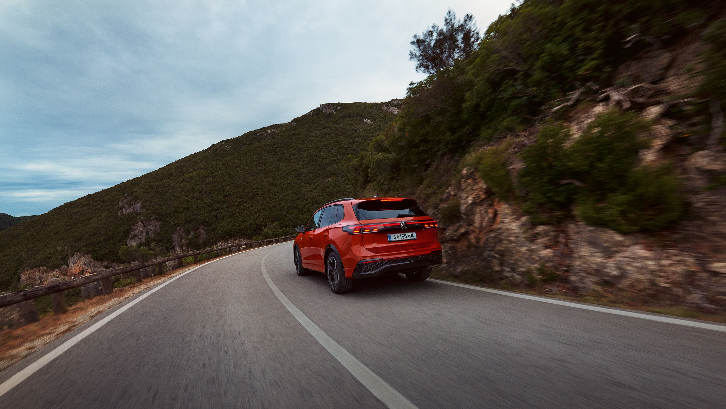 Roter VW Tiguan in Heckansicht fährt durch eine bergige Landschaft.