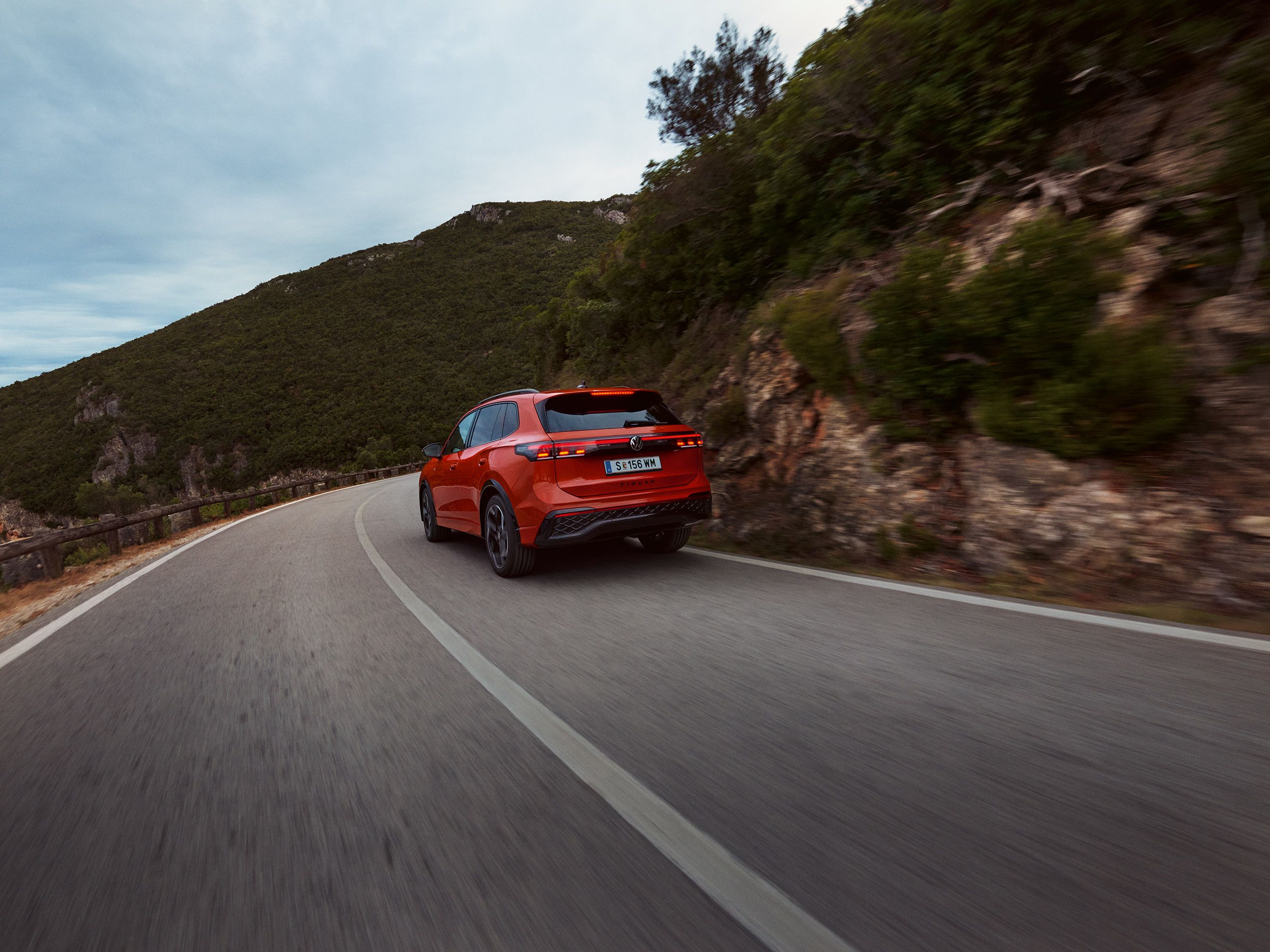 Roter VW Tiguan in Heckansicht fährt durch eine bergige Landschaft.