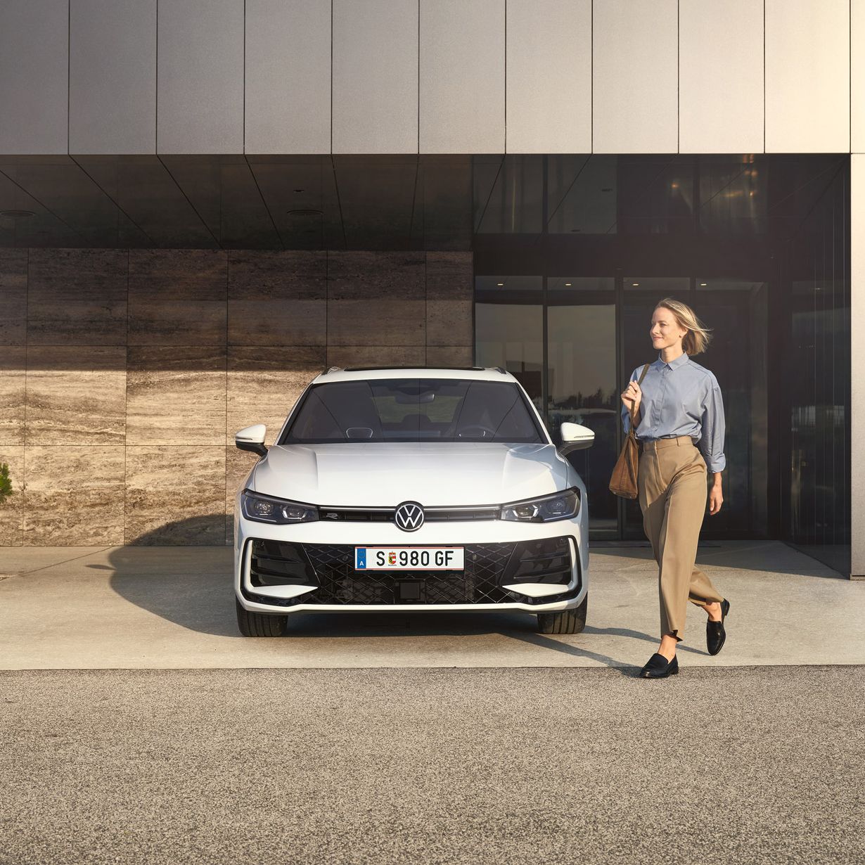 Frontansicht eines weißen VW Passat R-Line, eine Frau geht an ihm vorbei.