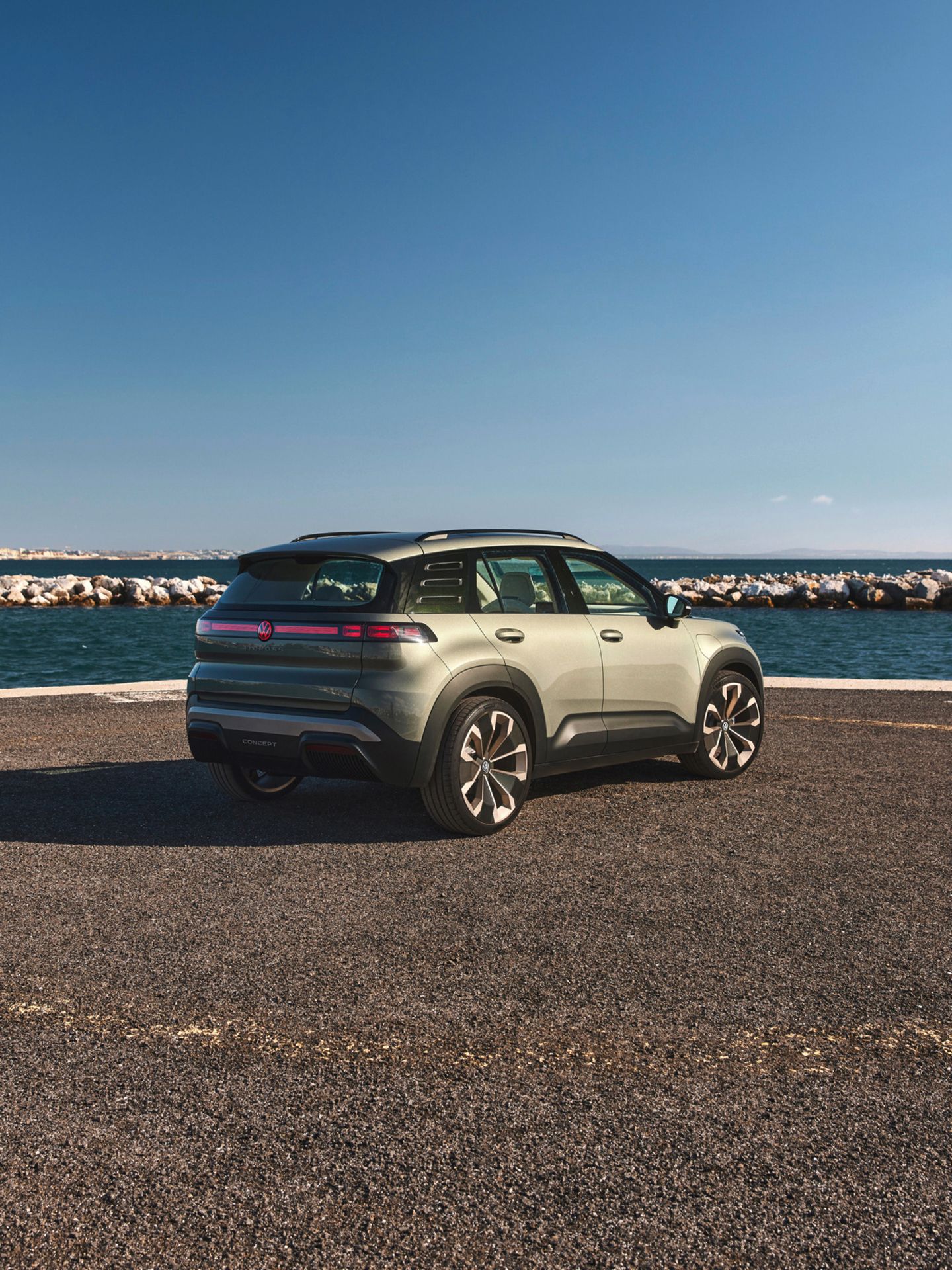 Ein grüner VW ID. Cross steht auf einer Küstenstraße mit Blick auf das Meer und einen blauen Himmel ohne Wolken. Im Hintergrund sind Felsen zu sehen, die das Meer abgrenzen.
