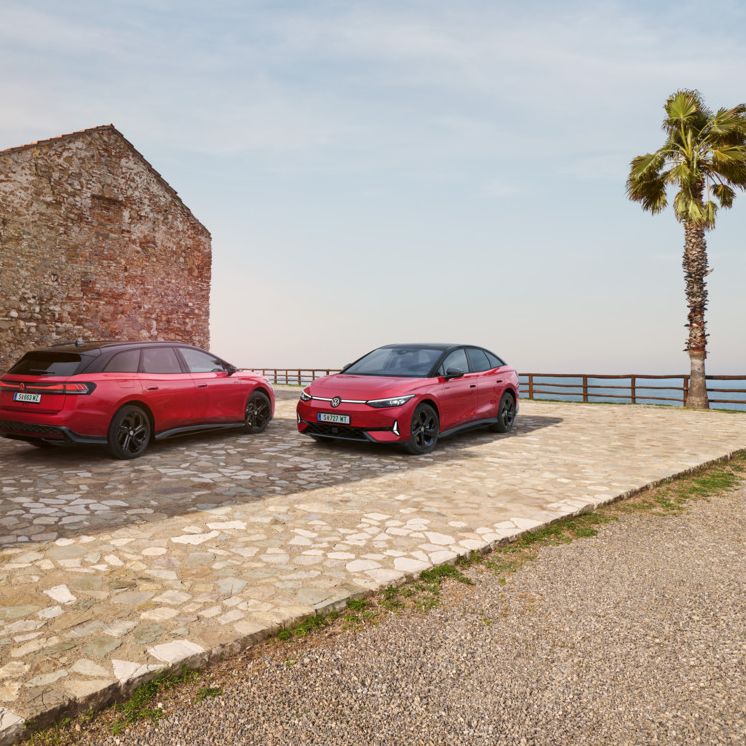 Ein roter ID.7 GTX und ID.7 Tourer GTX stehen nebeneinander vor einem Steinhaus mit Bick auf das Meer. 