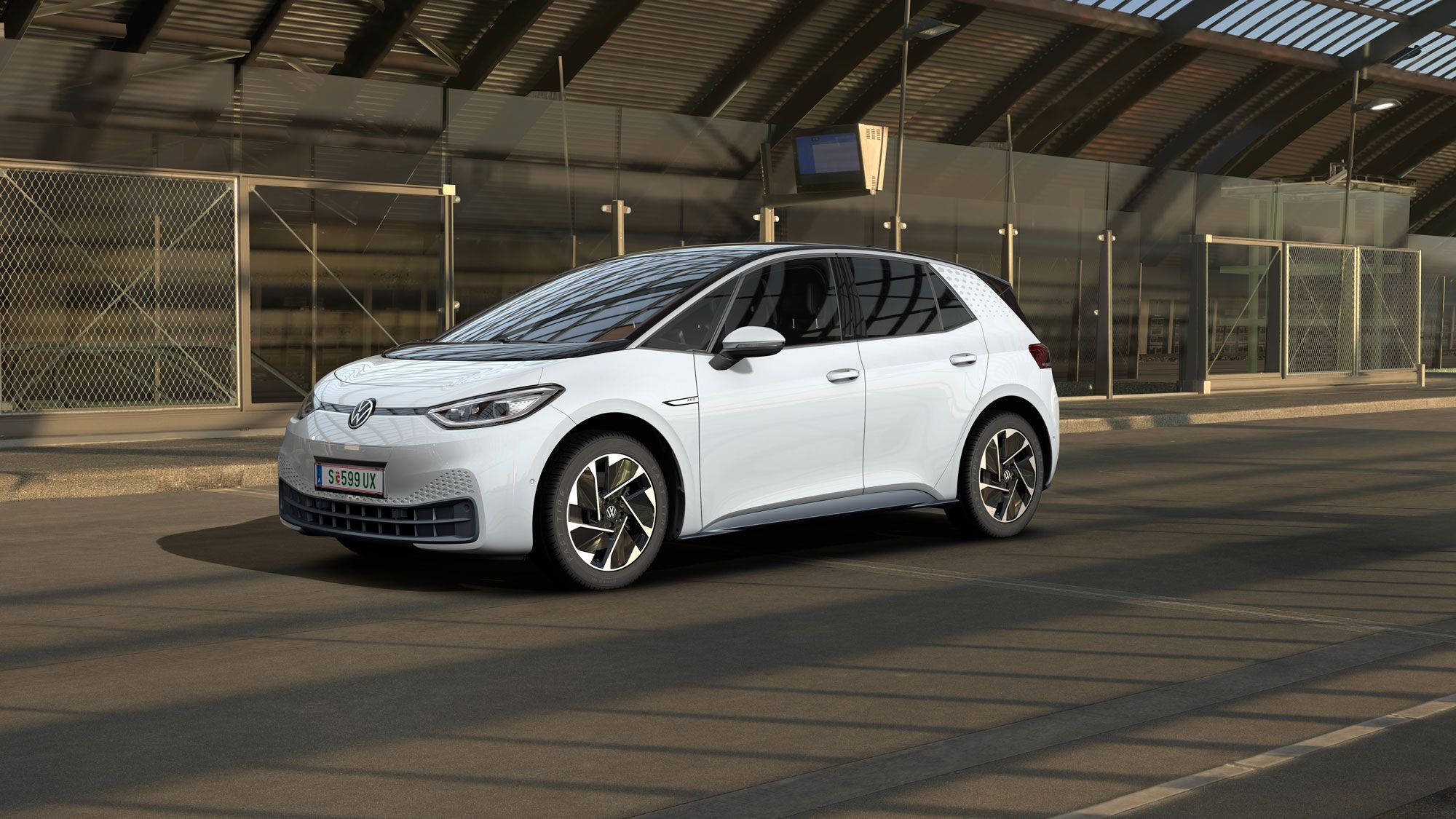 Ein weißer Volkswagen ID.3 steht in einer modernen, teilweise verglasten Tiefgarage. Das Auto ist von der Seite und leicht von vorne zu sehen. Im Hintergrund sind Maschendrahtzäune und Betonwände zu erkennen.