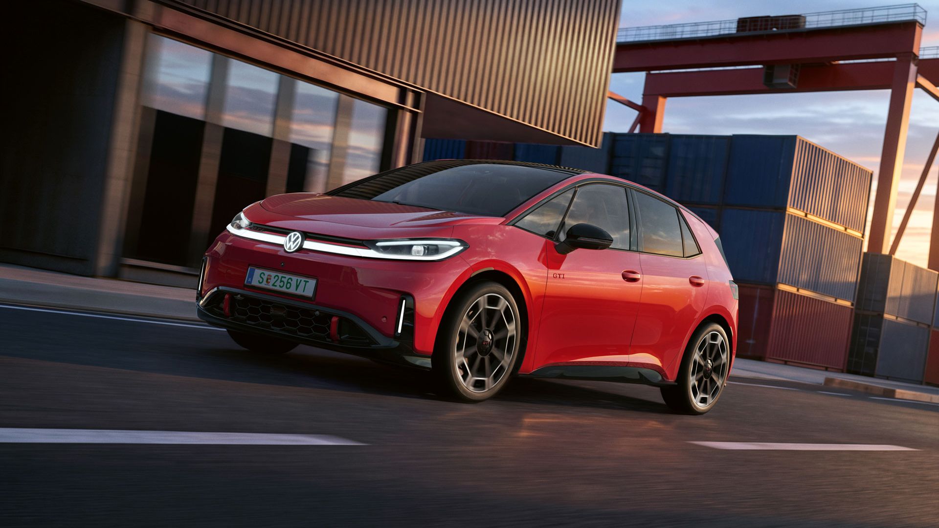[AI-modified] – Ein roter VW ID.3 GTI fährt mit eingeschalteten Scheinwerfern und beleuchtetem Logo an einem Hafengebäude vorbei.