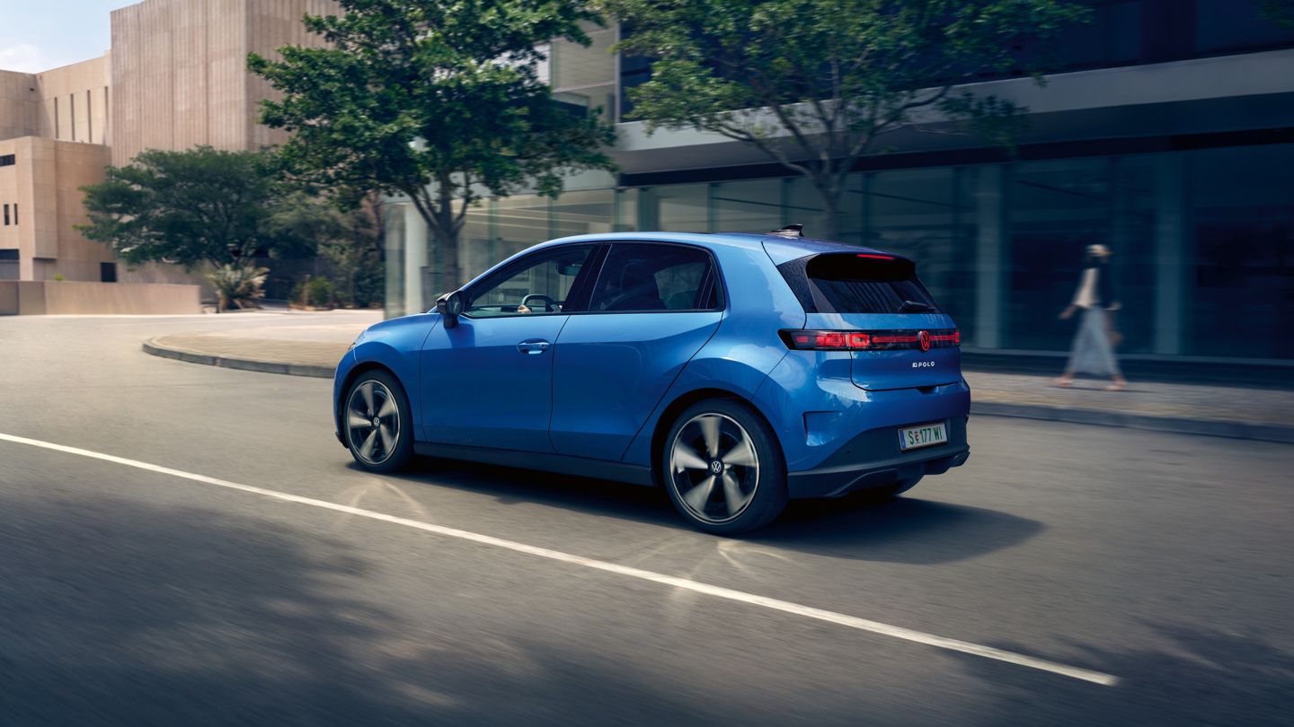 Ein blauer VW ID. Polo Style fährt durch eine Stadt mit grünen Bäumen am Straßenrand.