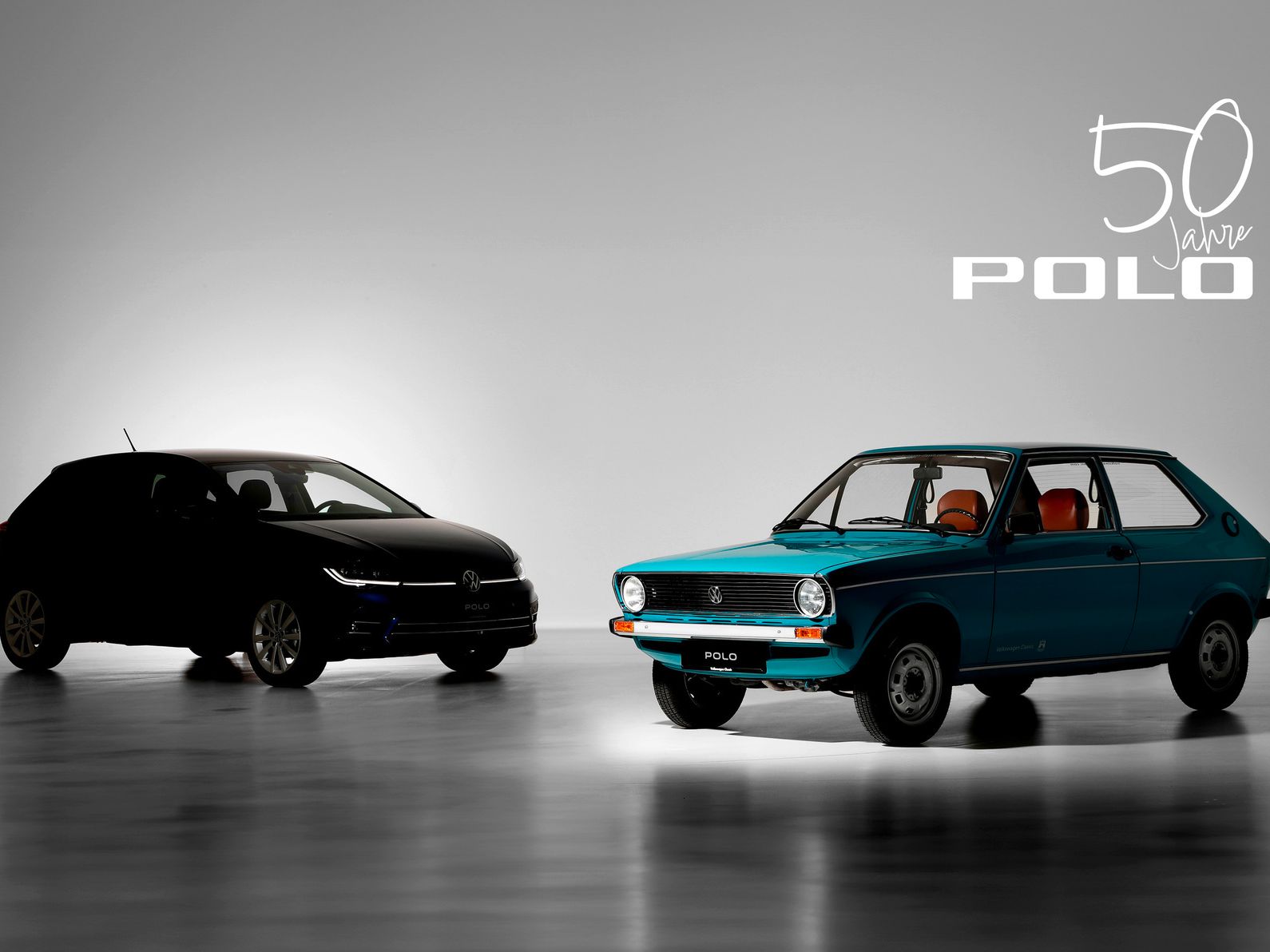 Zwei Volkswagen Polo Modelle nebeneinander: ein moderner schwarzer Polo und ein klassischer blauer Polo aus den frühen Jahren. Im Hintergrund steht „50 Jahre Polo“ geschrieben. Beleuchtung betont die Unterschiede zwischen den beiden Fahrzeugen.