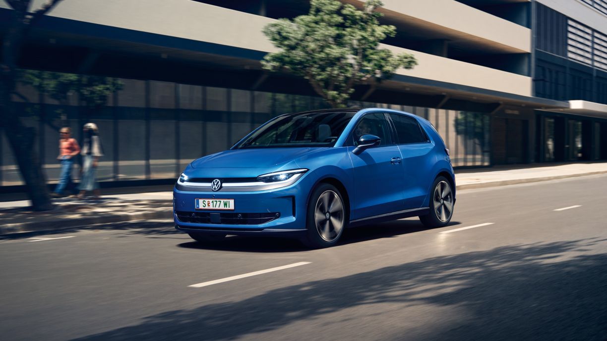Ein blauer VW ID. Polo Style fährt durch eine Stadt mit grünen Bäumen am Straßenrand.