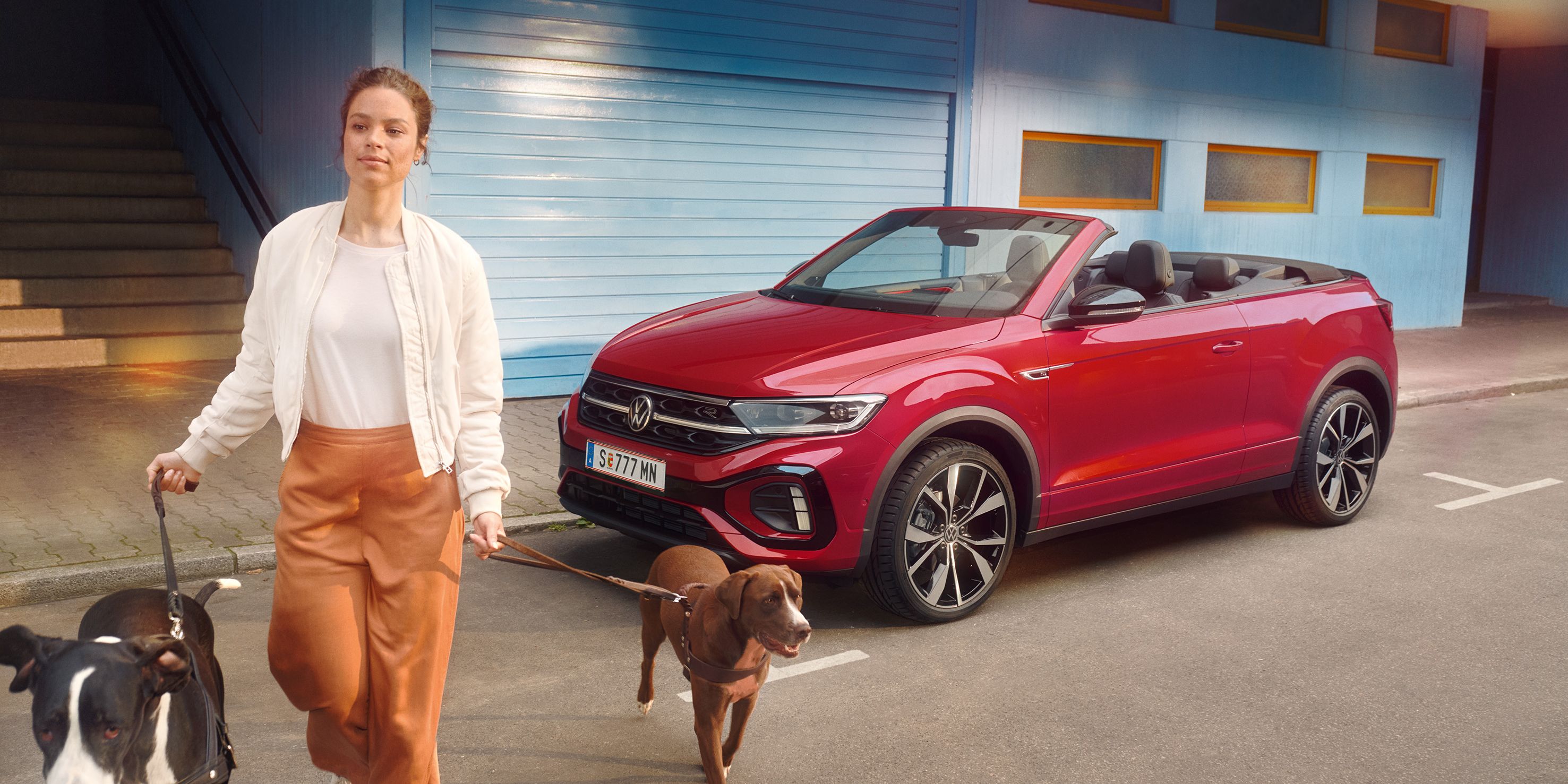 Frau geht mit zwei Hunden and der Leinen von einem roten VW T-Roc Cabrio weg
