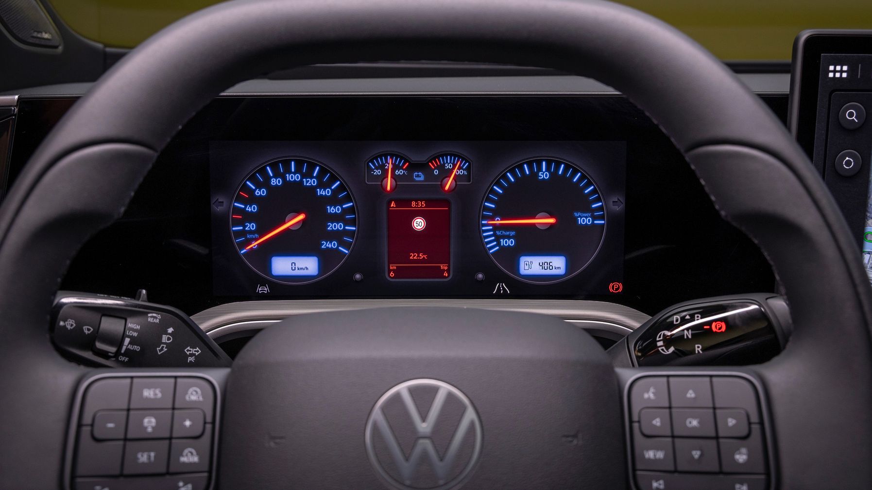 Nahaufnahme eines Volkswagen-Lenkrads mit digitalem Armaturenbrett und leuchtenden Instrumentenanzeigen. Links ist der Drehzahlmesser, rechts der Tacho, in der Mitte ein Display mit Warnsymbolen und Fahrzeuginformationen. Am Lenkrad befinden sich zahlreiche Bedientasten für Assistenzsysteme, Audio und Navigation.