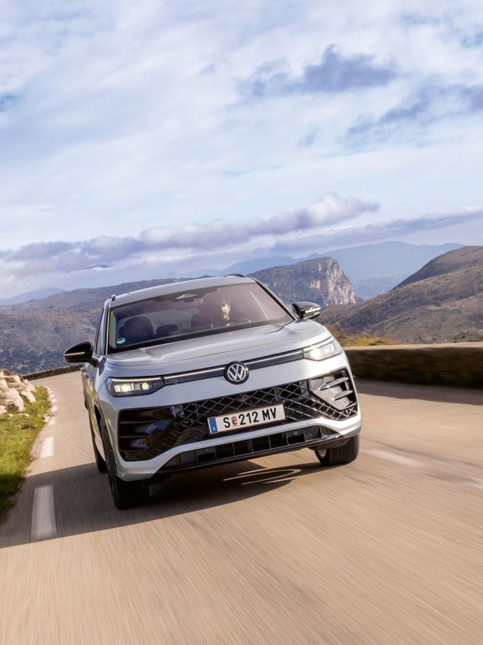 Tayron fährt auf einer Bergstraße, im Hintergrund befinden sich 
