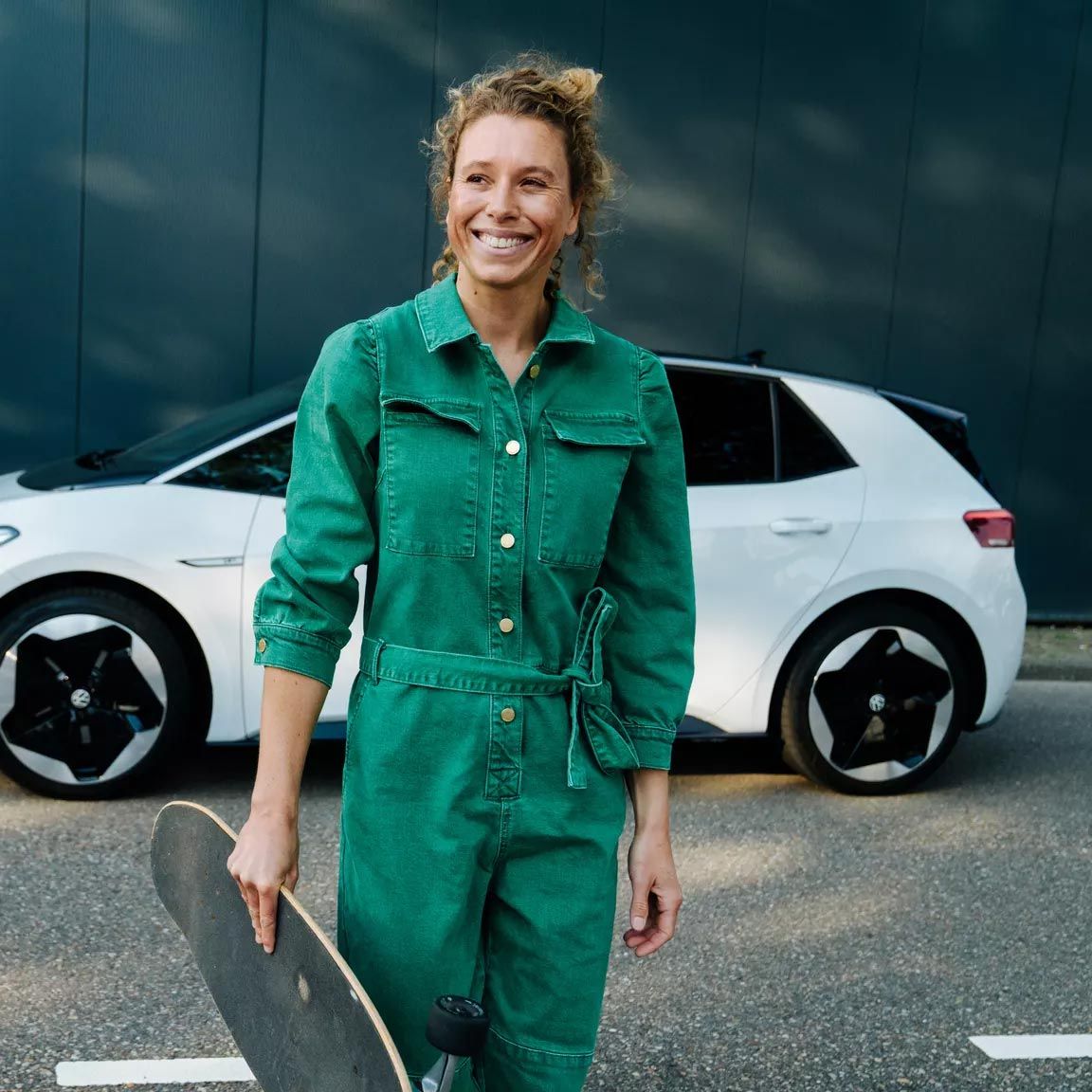 Frau mit Skateboard vor Elektroauto