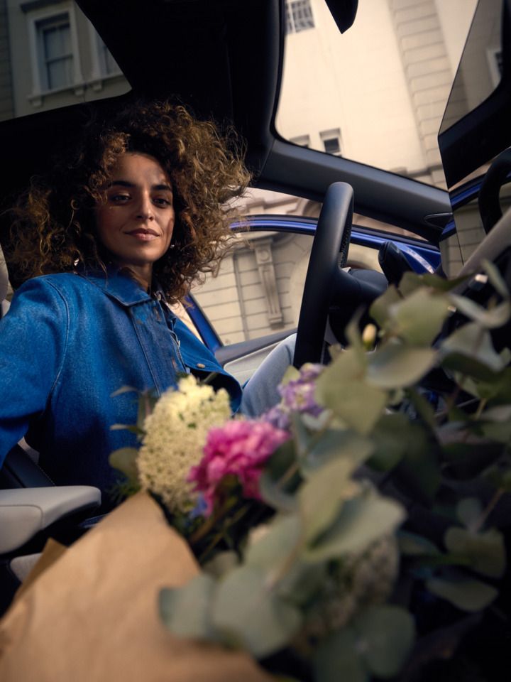 Eine Frau sitzt auf dem Fahrersitz eines blauen VW ID.Polo Style und greift nach einem Blumestrauß auf dem Beifahrersitz.