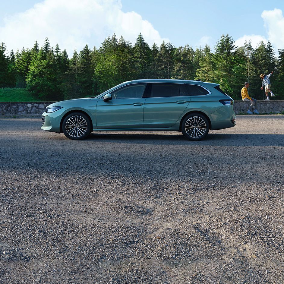 Seitenansicht eines grünen VW Passat Elegance vor einem Wald, im Hintergrund sieht man einen Mann und einen Jungen.