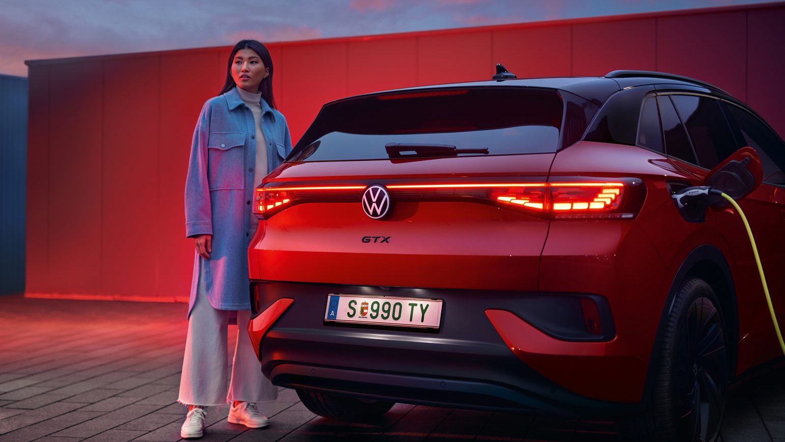 Heckansicht des VW ID.4 GTX 4MOTION, eine Frau steht daneben