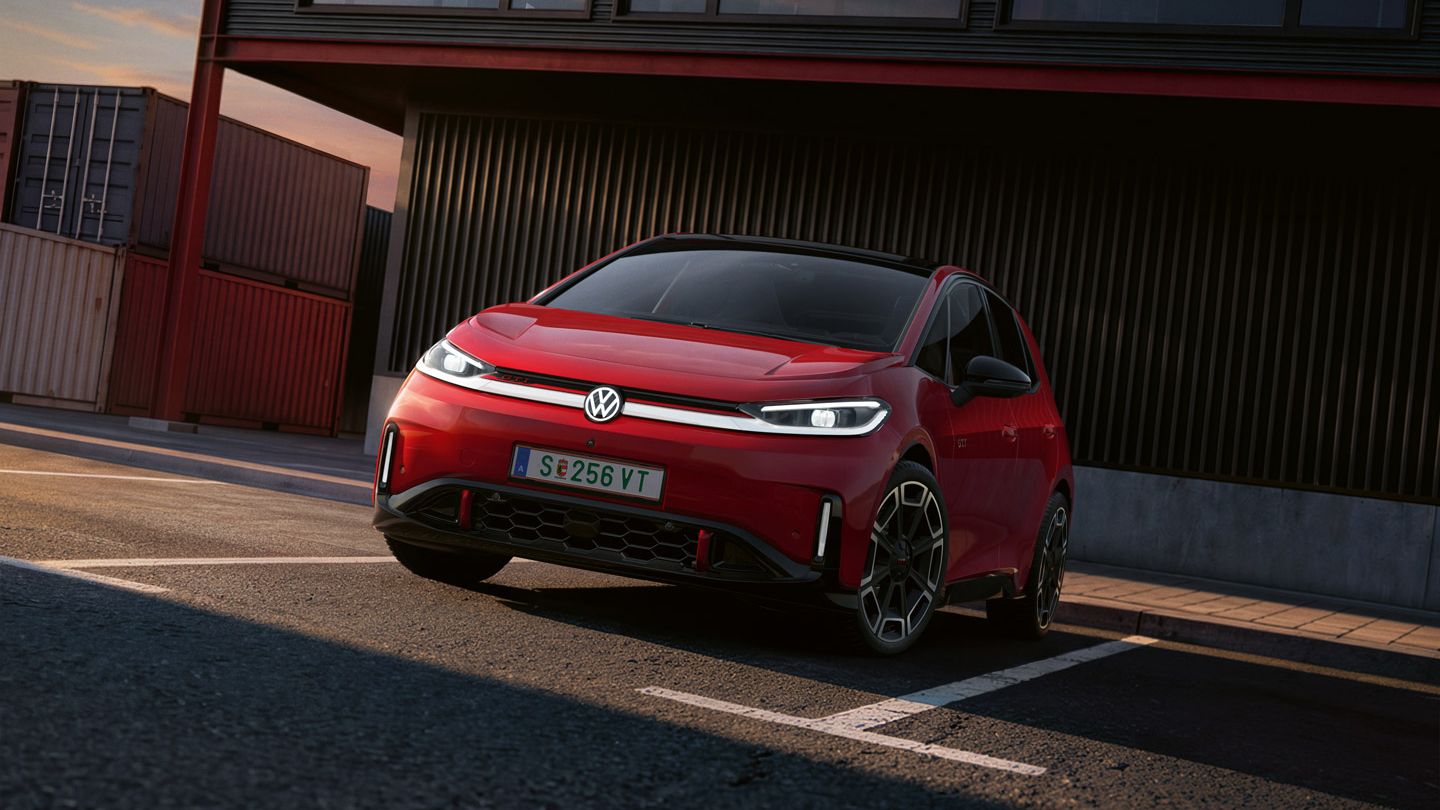 [AI-modified] – Frontansicht eines roten VW ID.3 GTI mit eingeschalteten Scheinwerfern und beleuchtetem Logo vor einem Gebäude.