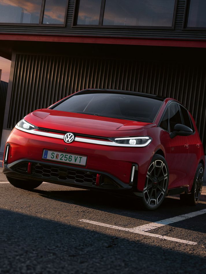 [AI-modified] – Frontansicht eines roten VW ID.3 GTI mit eingeschalteten Scheinwerfern und beleuchtetem Logo vor einem Gebäude.