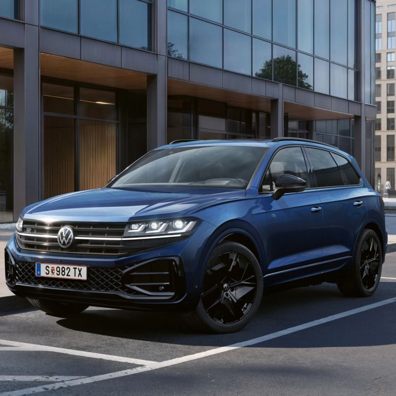 Ein blauer VW Touareg Final Edition steht vor einem Bürogebäude mit Glasfassade - Ansicht von schräg vorne.
