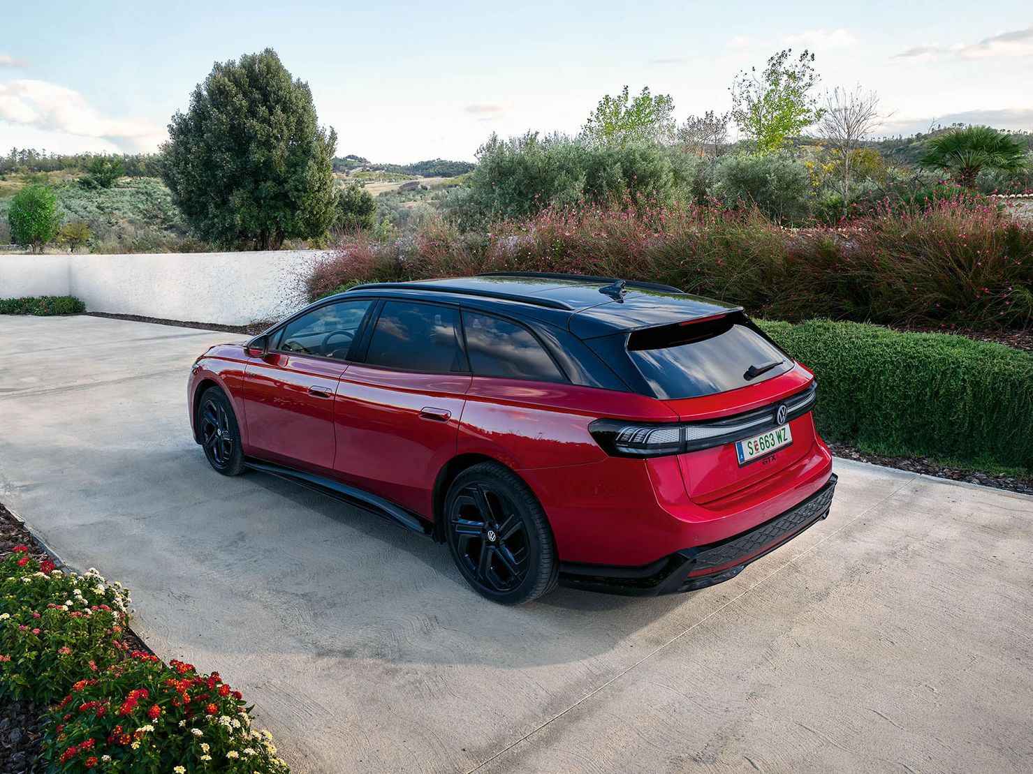 Ein roter VW ID.7 GTX Tourer parkt in einer Auffahrt mit Bäumen im Hintergrund.