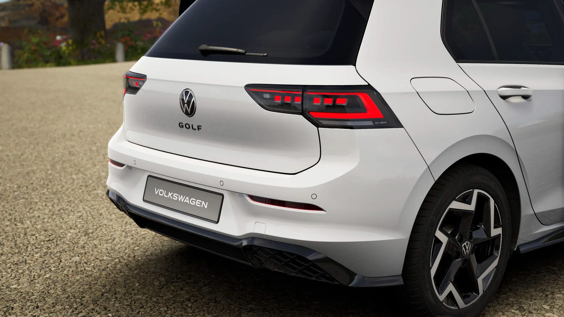 Rückansicht eines weißen Volkswagen Golf, geparkt auf einer Kiesauffahrt. Die Heckleuchten sind markant und das Emblem sowie der Schriftzug "Volkswagen" sind sichtbar. Die Felgen sind schwarz gehalten.