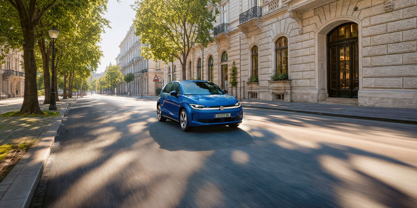 Ein blauer VW ID. Polo fährt auf einer breiten Straße im Schatten einer Allee.