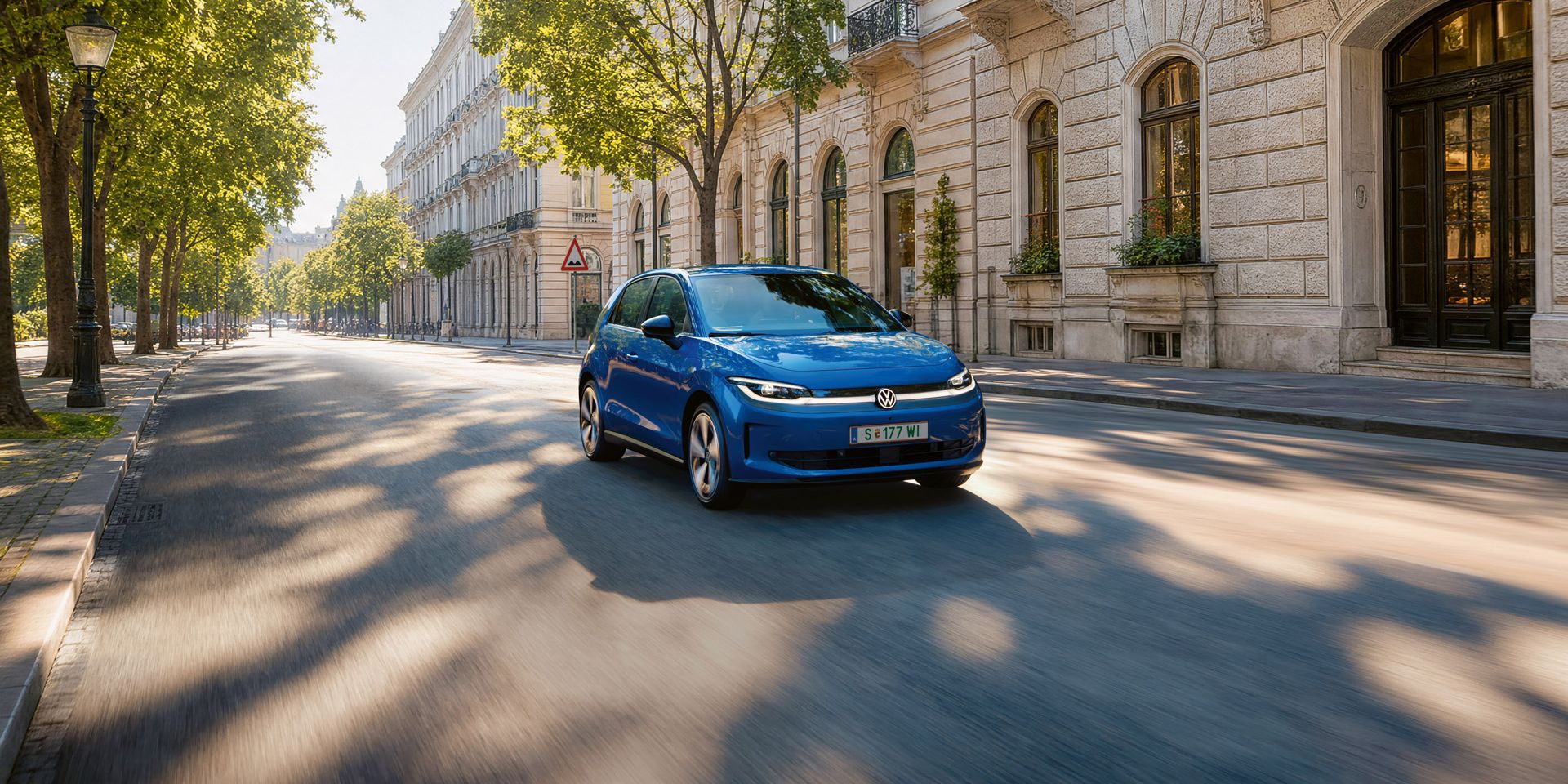 Ein blauer VW ID. Polo fährt auf einer breiten Straße im Schatten einer Allee.