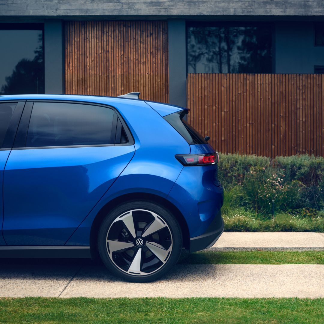 Seitliche Heckansicht eines blauen VW ID. Polo Style, der vor einem Wohnhaus mit begrünter Einfahrt steht.