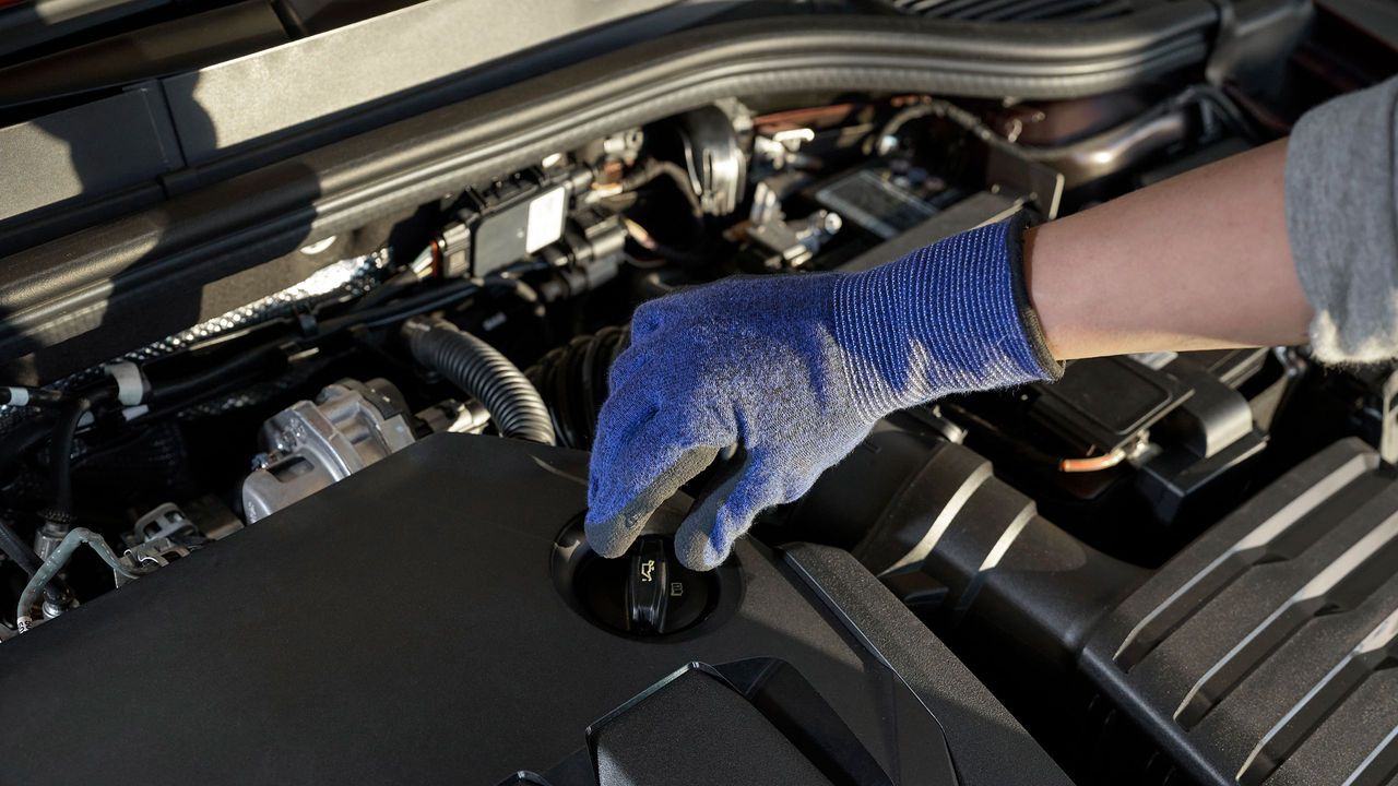 Block in den Motorraum eines Volkswagen. Eine Hand greift zum Ölmessstab.