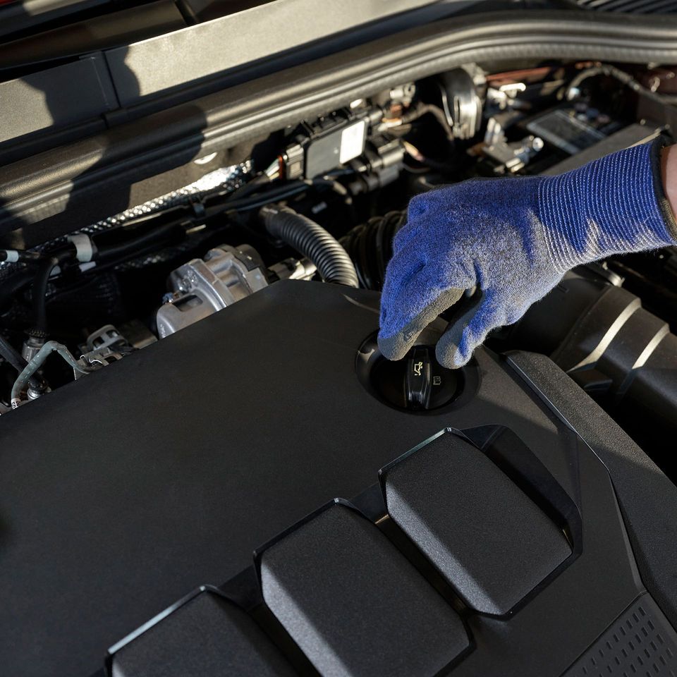 Block in den Motorraum eines Volkswagen. Eine Hand greift zum Ölmessstab.