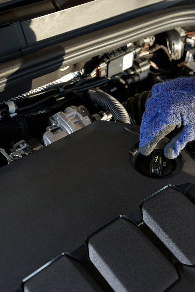 Block in den Motorraum eines Volkswagen. Eine Hand greift zum Ölmessstab.